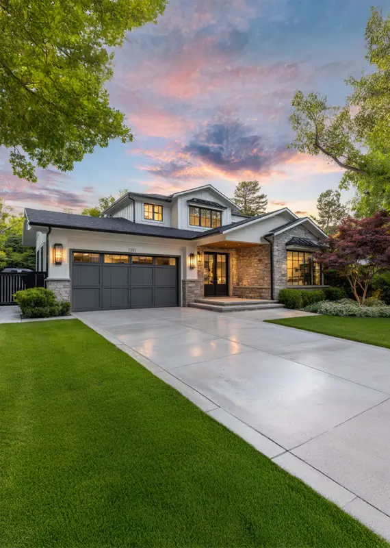 High-end home with a large garage and a gray steel gate, green grass in the front yard, a sunset, a light pink sky, a white concrete driveway.
